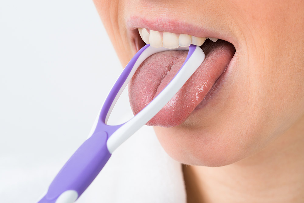Woman using a tongue scraper to clean her tongue.