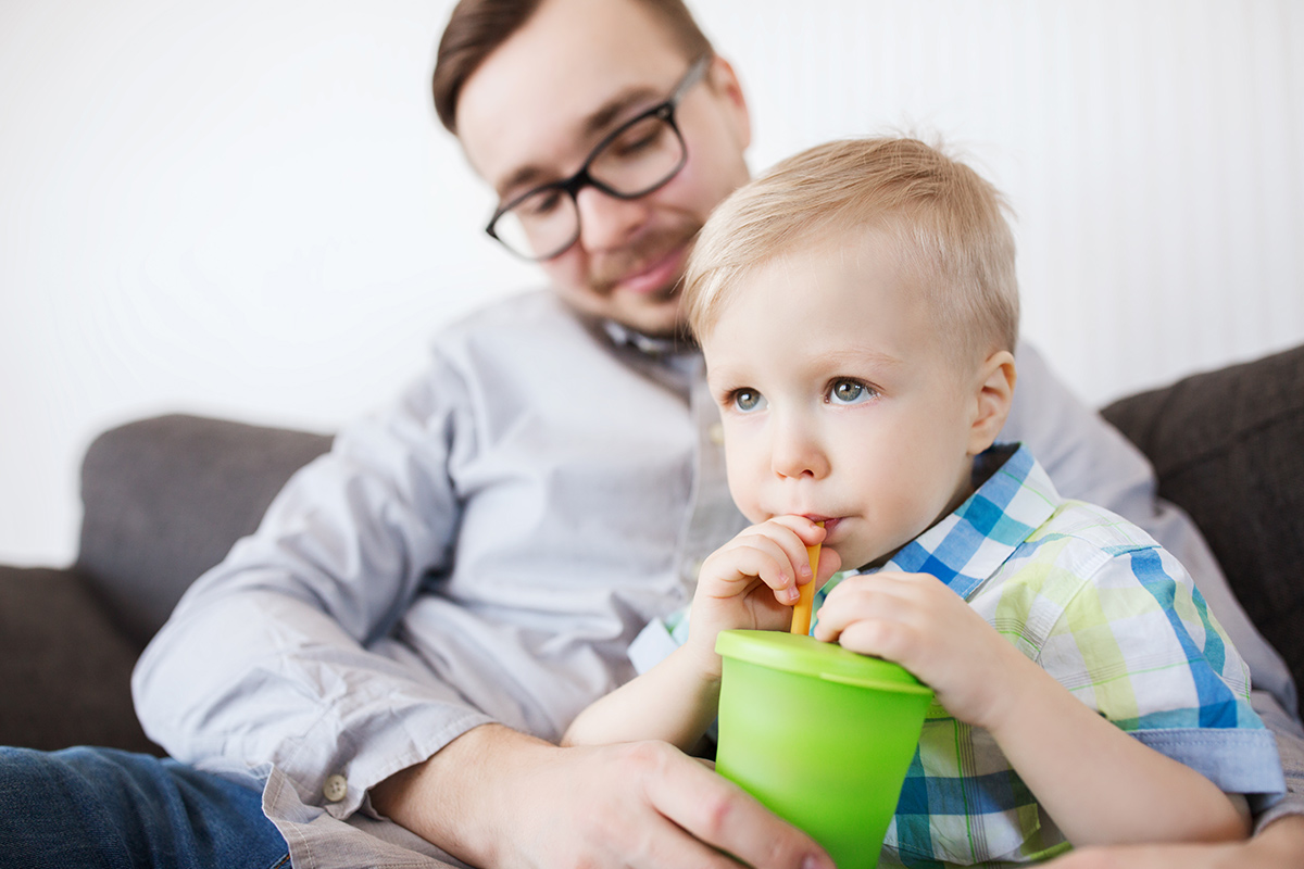 Father with son drinking through a straw from a plastic cup.
