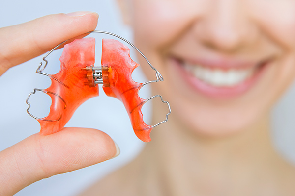 Smiling woman holding an orthodontic retainer between her fingers.