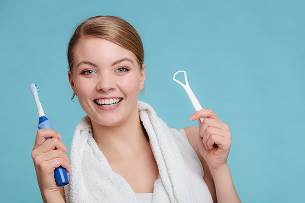 Woman holding an electric toothbrush and tongue cleaner.