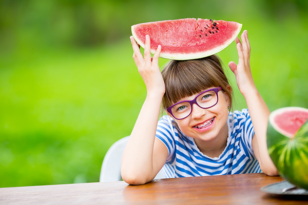 Girl holding a watermelon after getting summer braces.