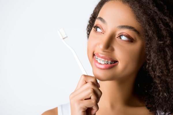 A girl with braces holds her toothbrush and smiles. Brushing with braces takes practice but it pays off with a winning smile.