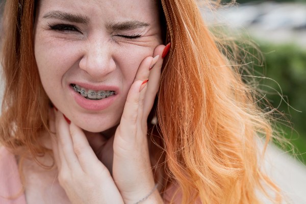 A woman with braces holding her mouth due to cuts from braces causing pain